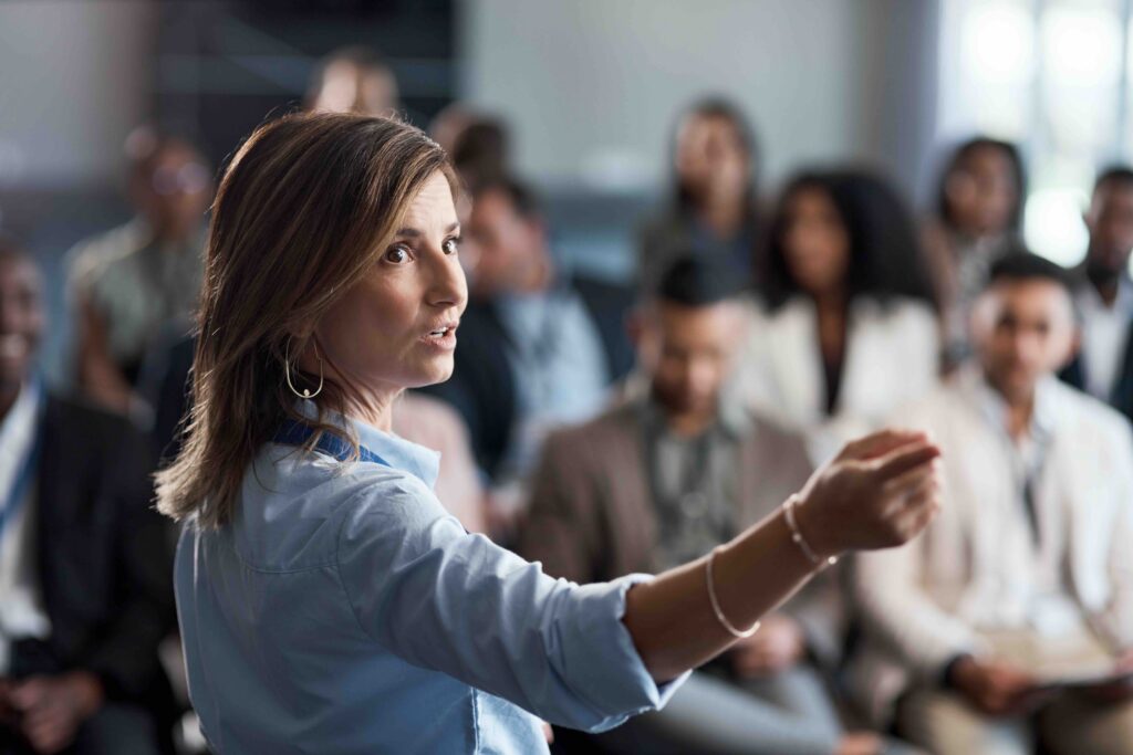 This image shows a woman presenting to a group in a professional setting.